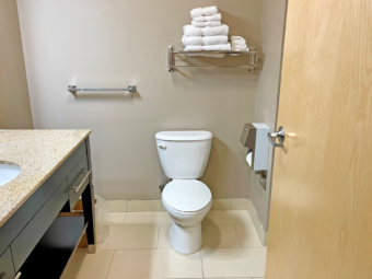 Vanity unit, towel rail and shelf with towels, toilet, tiled flooring