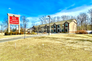 Hotel entrance with drive through canopy, two story building, parking spaces, grassy areas landscaping with small shrubs and trees