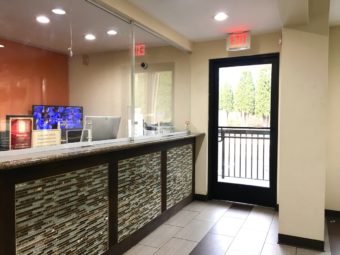 Guest check in reception desk with sliding glass screens, glass door leading to hotel exterior, tiled flooring
