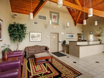 Hotel lobby featuring high wooden ceiling with beams, wall mounted art, sofa, easy chairs, artifical tree, rug, coffee table, front desk for check in and tiled floor