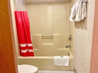 Toilet, shower tub with shower curtain and bathmat, towel rail with towels, tiled flooring