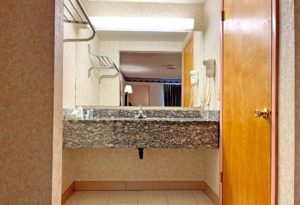 Vanity unit with overhead lighting and hairdryer, shelf with hanging rail, door to bathroom, tiled flooring