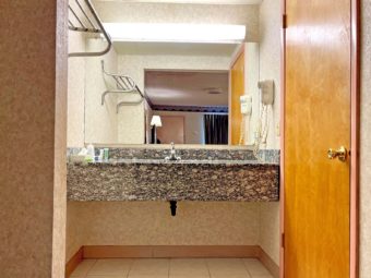 Vanity unit with overhead lighting and hairdryer, shelf with hanging rail, door to bathroom, tiled flooring