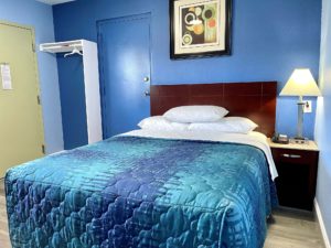 Queen bed, art image, night stand with telephone and bedside lamp, hanging rail with hanger and overhead shelf, laminate flooring