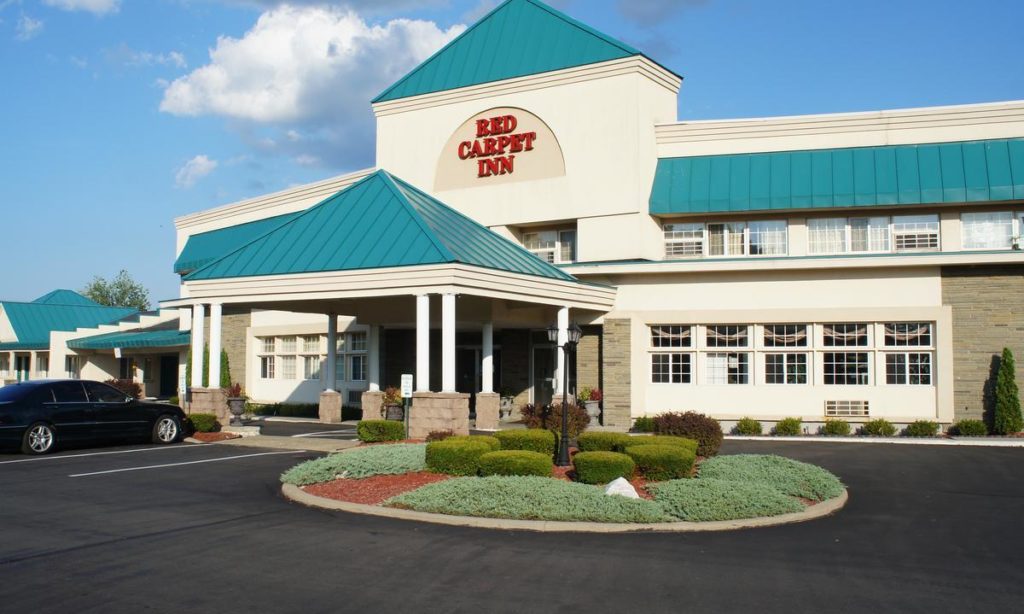 Hotel entrance with canopy, two story building, parking spaces, landscaping with small trees and trimmed bushes