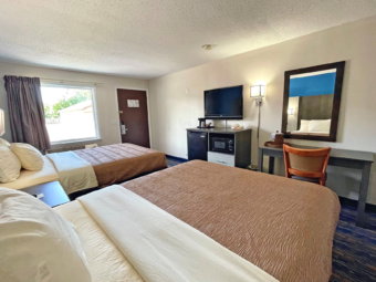 Two queen beds, night stand, wooden unit with coffee maker, fridge and microwave, wall light, mirror, desk with chair, carpet flooring