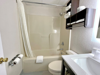 Shower tub with shower curtain, bath mat, toilet, towl storage with towels, vanity unit, illuminated mirror