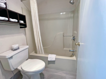 Shower tub with shower curtain, bath mat, toilet, towel storage with towels, tiled flooring