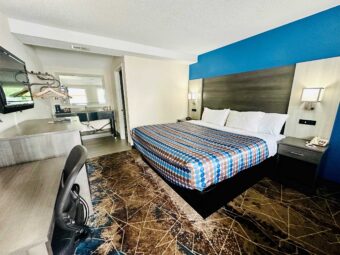 king bed, night stands with clock and telephone, wall bedside lights, desk and office chair, wooden drawer unit, wall mounted TV, hanging rail with hangers, alcove with vanity unit with coffee maker and mirror, carpet flooring