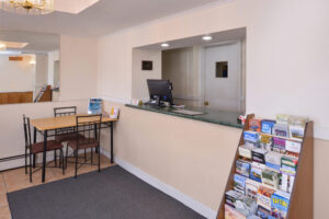 Guest check in desk, guest information leaflet stand, tables and chairs, large wall mounted mirror, mat and tiled flooring