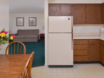 Full size fridge, table with chairs, wall mounted and base cabinets, tiled flooring, doorway to sofa, wall mounted art, carpet flooring