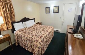 King bed, night stands with clock, art images, wooden drawer units with TV and telephone, carpet flooring
