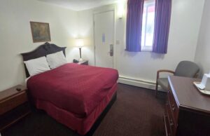 Queen bed, night stands with bedside lamp and telephone, art image, chair, wooden drawer unit, carpet flooring