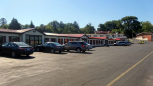 One story building, parking spaces, large trees in the background