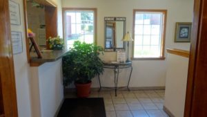 Guest check in desk, potted plant, wall mounted mirror, occasional table with lamp and guest information, tiled flooring