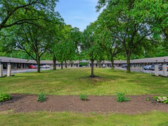 one story building with exterior guest room entrances, parking spaces, grassy area with trees