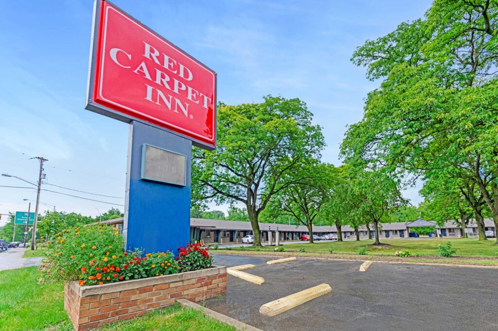 Brand signage, one story building with exterior guest room entrances, parking spaces, grassy area with trees
