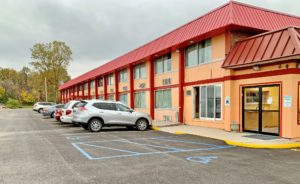 Hotel entrance, two story building, parking spaces, trees and grassy area at end of parking lot