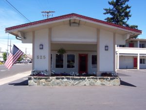 Hotel canopy entrance, stone flower beds with flowers, two story building and parking spaces