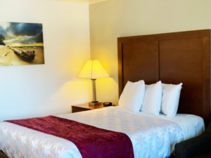 Queen bed, night stand with bedside lamp and clock, sofa, art image