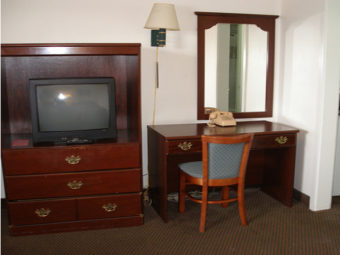 Wooden TV console unit with tv, desk with chair and telephone, wall mounted light, wall mounted mirror, carpet flooring