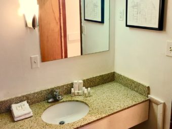 Vanity unit with sink, bathroom amenities, wall mounted mirror and light