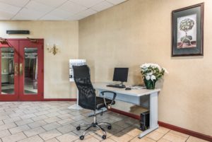 Double doors leading to restaurant, desk with monitot, keyboard and potted plant, office chair, art image, tiled flooring