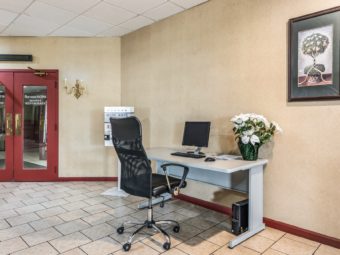 Double doors leading to restaurant, desk with monitot, keyboard and potted plant, office chair, art image, tiled flooring