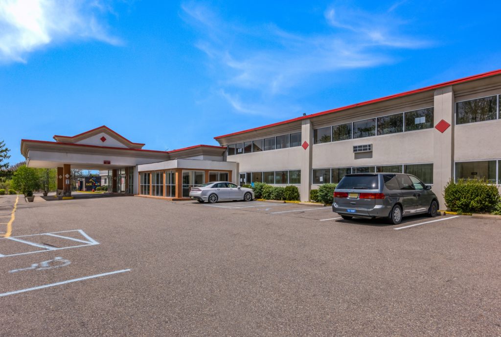 Hotel canopied drive through entrance, two story building, small bushes and trees, parking spaces