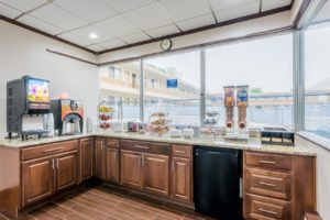 Breakfast display counter with base cabinets and fridge, juice machine, coffe machine, display case with breakfast pastries, cereal dispensers, tiled flooring