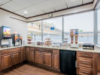 Breakfast display counter with base cabinets and fridge, juice machine, coffe machine, display case with breakfast pastries, cereal dispensers, tiled flooring