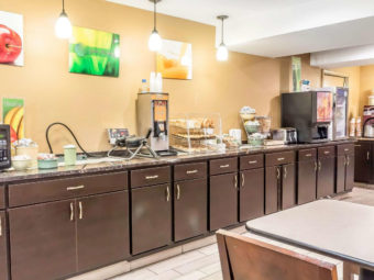 Breakfast display counter with microwavem waffle maker, breakfast pastries, juice dispenser, chilled cabinet with yogurts, coffe machine, tables and chairs, tiled flooring