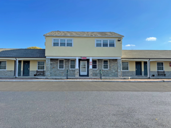 Hotel entrance. two story building with one story buildings either side with exterior room entrances, parking spaces