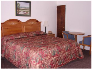 King bed, night stand with bedside lamp and telephone, wall mounted art, small table and two chairs, carpet flooring