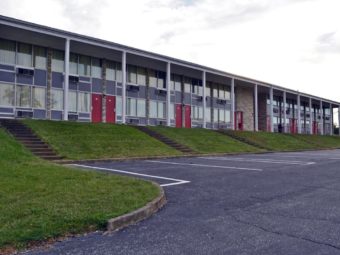 Hotel exterior, two story building with exterior room entrances on ground floor, steps leading to parking spaces, grassy areas