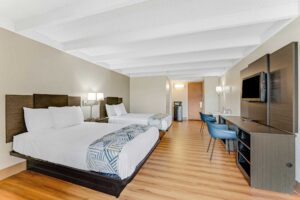 Two double beds, night stand with telephone, wall bedside lamps, wooden unit with TV and chair, desk with chair, fridge with microwave, laminate flooring