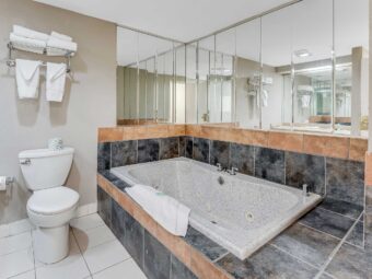 toilet, shelf and rail with towels, spa tub with mirrored surround