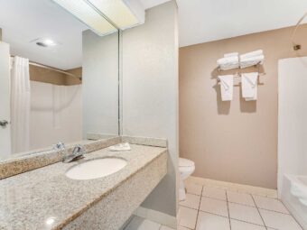 Vanity unit, mirror, toilet, shelf and rail with towels, shower tub, tiled flooring