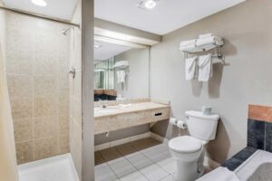 Shower with shower curtain, vanity unit, mirror, shelf and rail with towels toilet, spa tub, tiled flooring