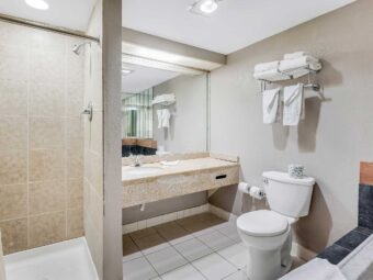 Shower with shower curtain, vanity unit, mirror, shelf and rail with towels toilet, spa tub, tiled flooring