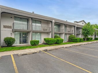 Two story building, balconies with sliding glass doors, landscaping with grassy areas and small bushes, parking spaces