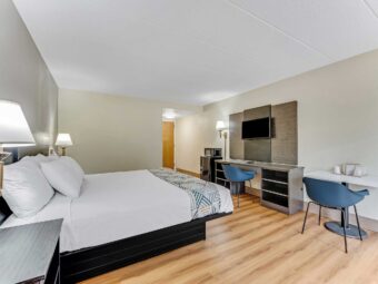 King bed, night stands, wall bedside lamps, wooden unit with TV, chair, desk with chair, fridge with microwave, wall light, laminate flooring