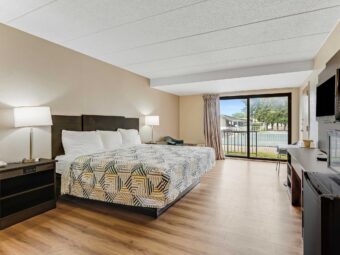 King bed, nightstands with bedside lamps, chair, wooden unit with TV, fridge with microwave, laminate flooring