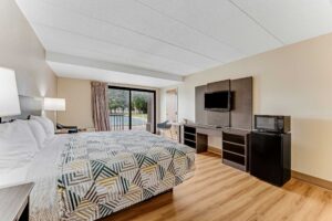 King bed, nightstands with bedside lamps, chair, wooden unit with TV, fridge with microwave, laminate flooring