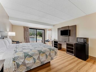 King bed, nightstands with bedside lamps, chair, wooden unit with TV, fridge with microwave, laminate flooring