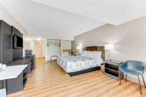 King bed, night stands with bedside lamps and telephone, chair, wooden unit with TV, fridge with microwave, hanging rail with hangers, folding portable luggage rack, laminate flooring