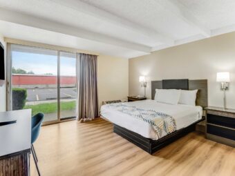 Queen bed, night stand with telephone, wall bedside lamps, unit with TV and chair, laminate flooring