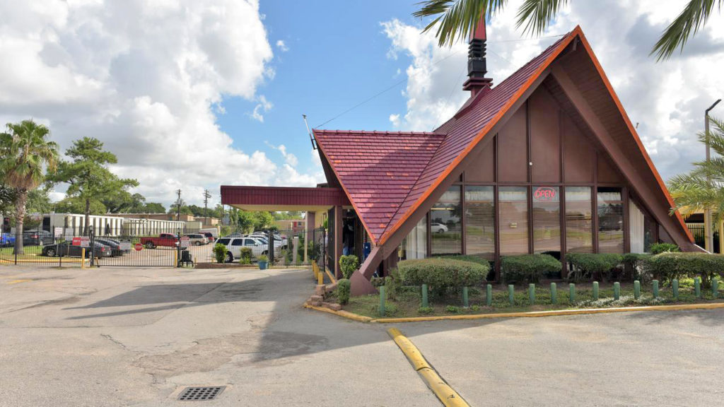 Hotel entrance with small canopy, gated area with exterior parking, small bushes and plants