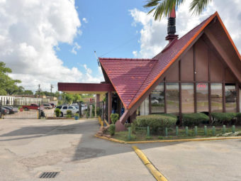 Hotel entrance with small canopy, gated area with exterior parking, small bushes and plants