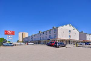 Three story building, brand signage, gated parking, grassy areas and small bushes